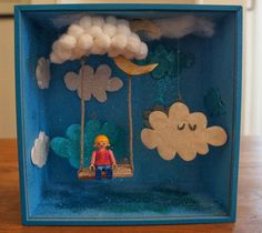 a blue box with clouds and a person sitting on a swing