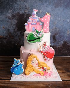 there is a three tiered cake with princesses on the top and castle in the background