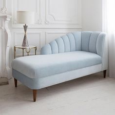 a blue chaise lounge chair sitting in front of a window with a lamp next to it