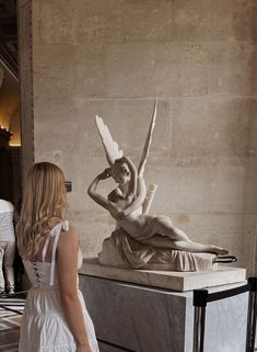 a woman standing next to a statue in a room with marble walls and flooring