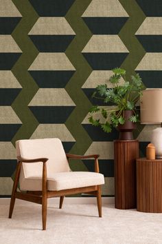 a chair and table in front of a wall with geometric designs on it, next to a lamp