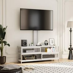 a flat screen tv sitting on top of a white entertainment center next to a potted plant