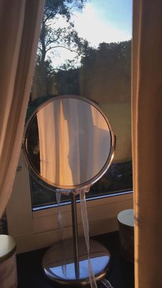 a round mirror sitting on top of a metal stand next to a window sill