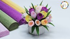 a vase filled with lots of colorful flowers next to rolled up fabric on top of each other