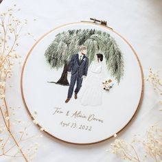 a wedding embroidered onto a white cloth with flowers and branches around it, next to a couple holding hands