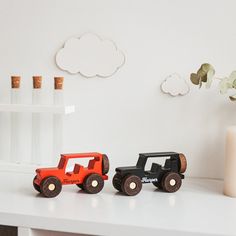 two toy trucks sitting on top of a white table next to a vase with flowers