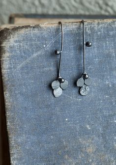 "This is a series which brings me much joy at the moment, light-weight black plant earrings in 925 silver. In this one, playful rivets and kinetic elements create a shape which is organic and abstract while dainty, delicate and beautiful in the ear. An unusual, elegant, delicate botanical pair. Oxidised to black and polished in a rotary tumbler for durability and shine. Subtle contrasts between texture and smoothness, achieved by the careful hammering of the dangles. These are small threader ear Hammered Metal Jewelry, Kinetic Earrings, Rivet Jewelry, Earrings Oxidised, Kinetic Jewelry, Organic Earrings, Plant Earrings, Handmade Silver Jewellery, Contemporary Jewelry Design