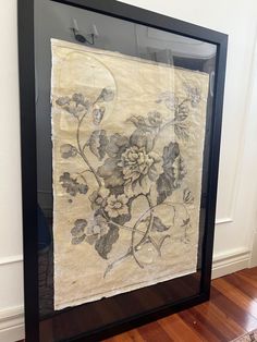 an old piece of paper with flowers on it in a frame next to a wall