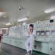 a woman in white jumpsuits standing next to a wall with electrical equipment on it