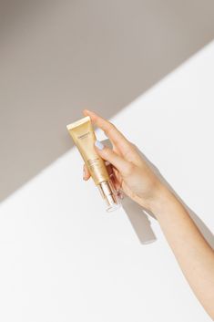 a hand holding a tube of cream on top of a white surface