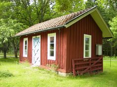 a small red cabin in the middle of a grassy field with trees and grass around it