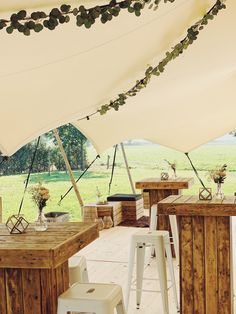 an outdoor dining area with tables and stools under a large white tent in the middle of a field