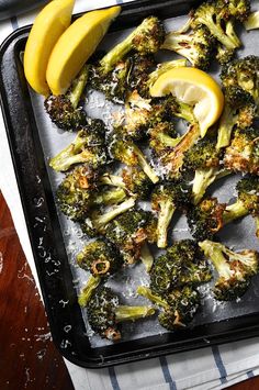 a tray filled with cooked broccoli and lemons on top of a table