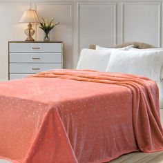 a bed with an orange bedspread on top of it and a white dresser