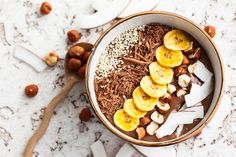 a bowl filled with chocolate and bananas on top of a white table next to nuts