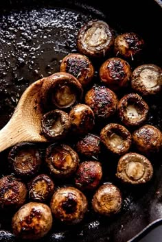 mushrooms cooking in a skillet with a wooden spoon on the side and oil running over them