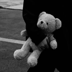 a person holding a teddy bear in their hands on the street with cars behind them