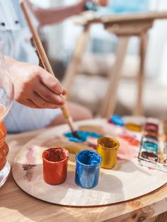 a person painting on a table with paints and brushes