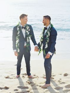 two men in tuxedos standing on the beach with leis around their necks