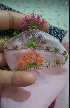 the hand is holding two small pieces of fabric with embroidered flowers on them, and one piece has been sewn