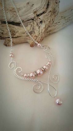 a necklace with pink pearls and silver wire on top of a piece of drift wood