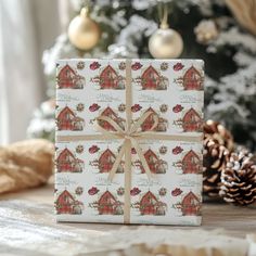 a christmas present wrapped in white paper with red barn designs on it and pine cones