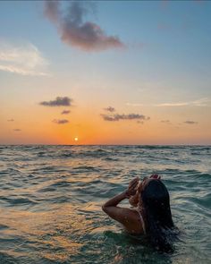 a woman in the ocean at sunset with her back to the camera, looking into the distance