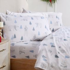 a bed with white sheets and blue trees on it, next to a night stand