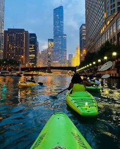 several kayakers are paddling down the river in front of tall buildings at night