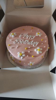 a pink birthday cake in a box with white and yellow flowers on the top that says happy birthday