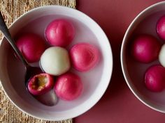 two bowls filled with red and white eggs on top of a pink table cloth next to a spoon