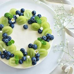 a white plate topped with a cake covered in blueberries, grapes and green leaves