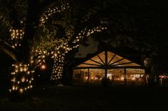 a lit up tent in the dark with people sitting at tables under lights and trees