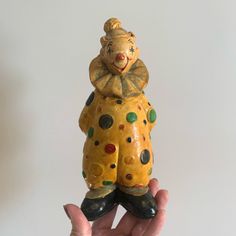 a hand holding a ceramic clown figurine in it's right hand, against a white background