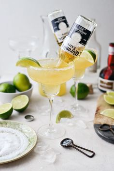 two glasses filled with lemonade and limes on top of a white tablecloth