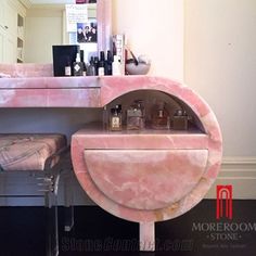 a pink marble vanity with stools in front of it and bottles on the counter