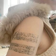 a woman with a tattoo on her arm that has sheet music written on it and she is looking at the camera