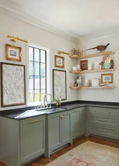 a kitchen with green cabinets and black counter tops in front of open shelves on the wall