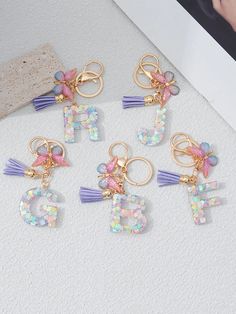 six charms with letters and tassels hanging from them on top of a table