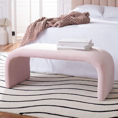 a pink bench sitting on top of a white rug next to a neatly made bed