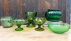 several green glass bowls and vases sitting on top of a wooden table next to each other