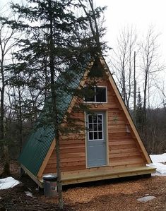 a small cabin in the woods with a green roof