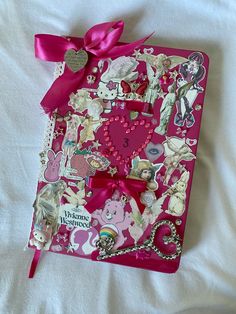 a pink book covered in lots of stickers and bows on top of a bed