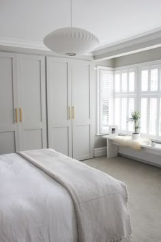 a white bed sitting in a bedroom next to a window filled with lots of windows