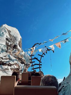 people are sitting in chairs looking up at the sky and mountains with flags hanging from them