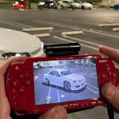 a person holding up a red camera to take a picture of a car on the street