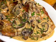 a white plate topped with meat covered in mushrooms and gravy next to lemons