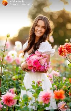 a woman in a white dress holding pink and red flowers with the sun behind her