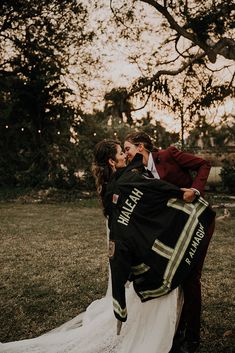 a bride and groom kissing under a blanket on their wedding day in the park at sunset