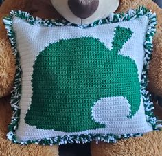 a crocheted teddy bear holding a pillow with a green design on it's face